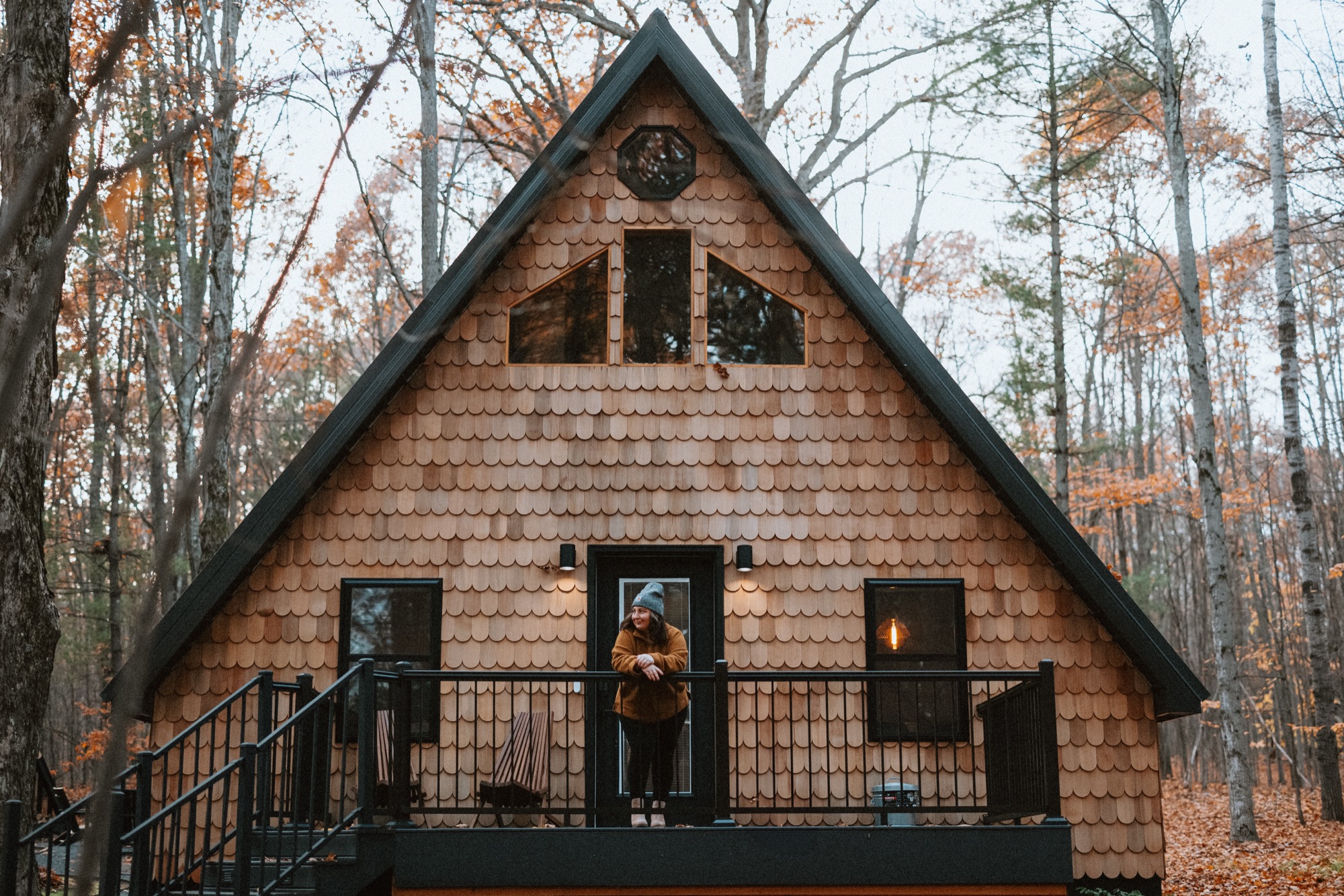 The Roost A-Frame cabin surrounded by fall foliage with warm interior light glowing from windows