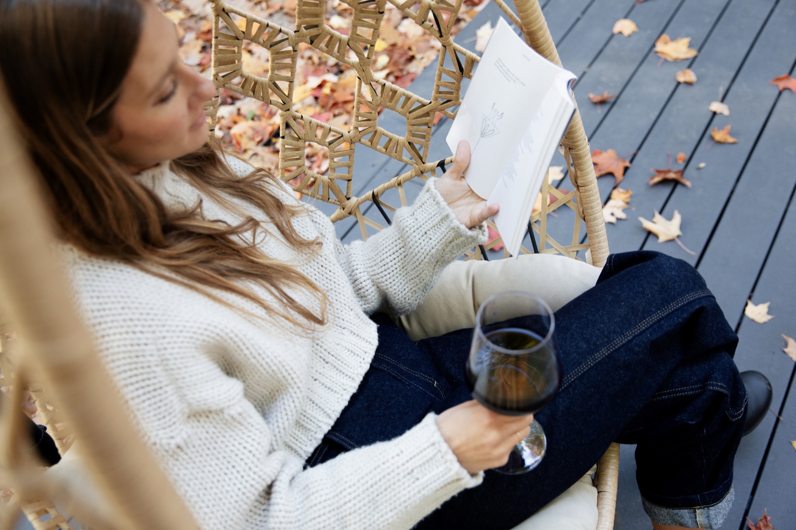 Woman relaxing in a hanging chair with a glass of wine on the A-frame cabin deck surrounded by fall leaves