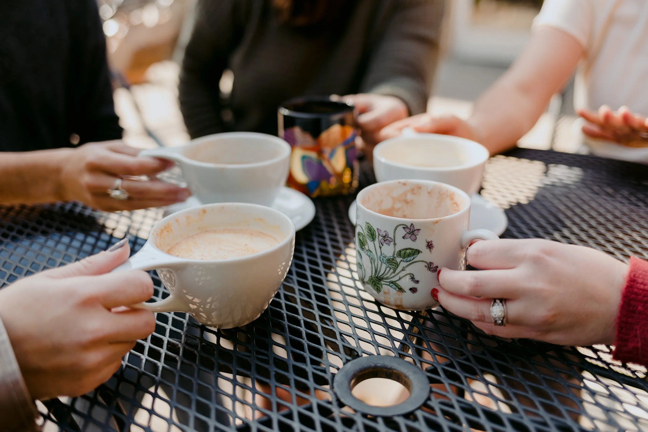 Friends clinking mismatched coffee mugs on an outdoor patio