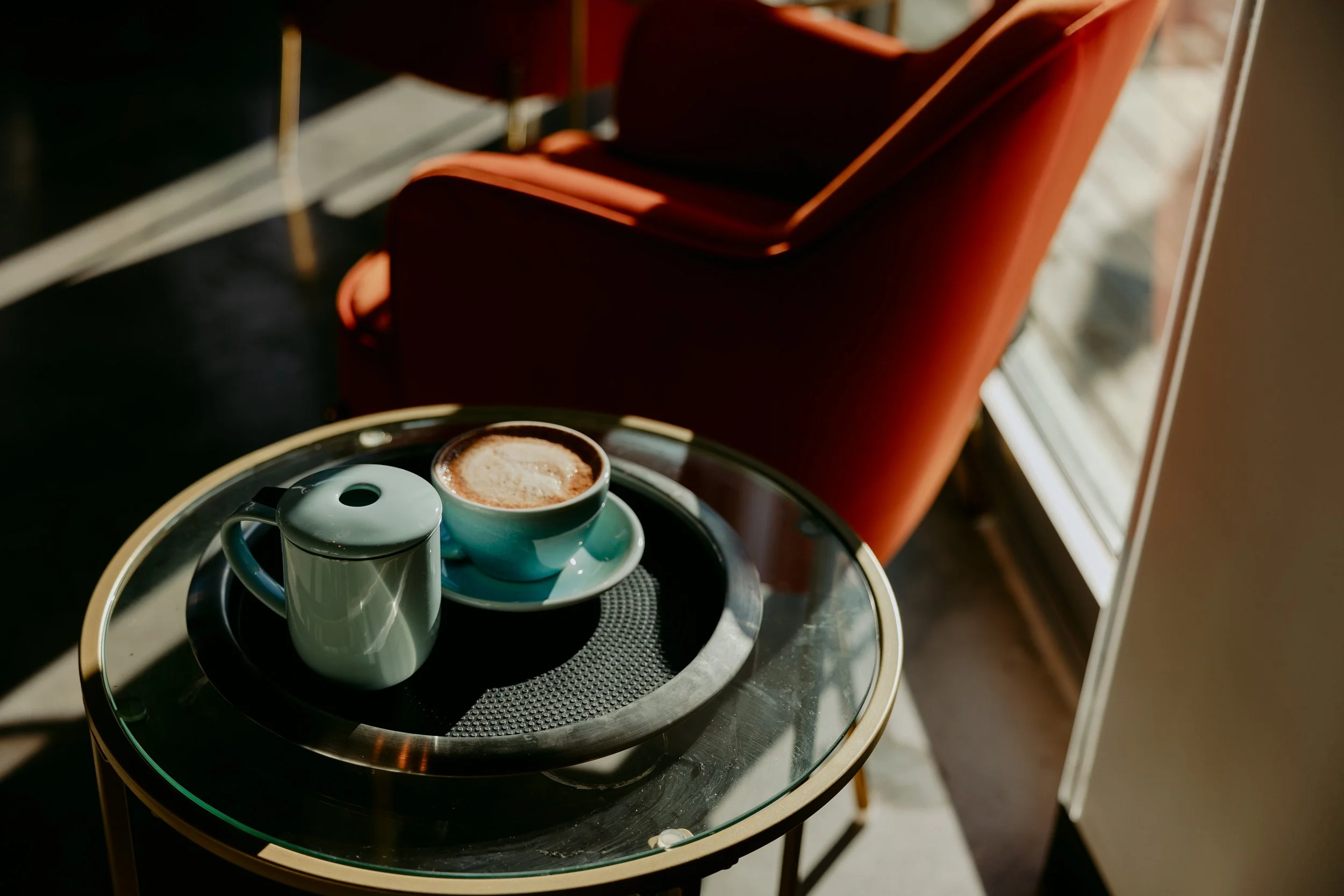 A latte with latte art on a side table next to a red velvet chair