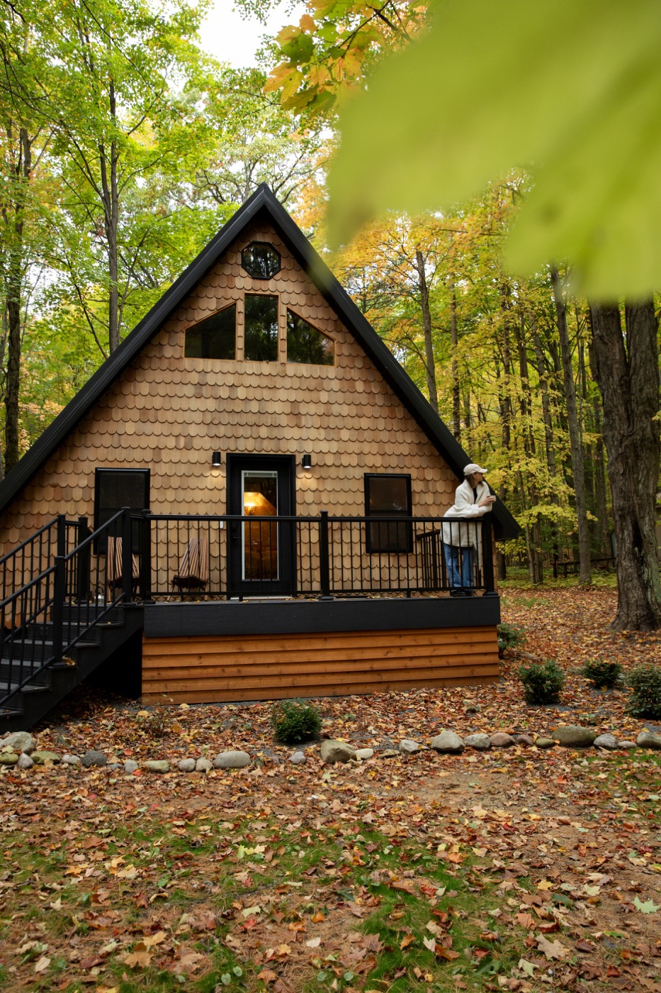 A modern A-frame cabin with cedar shake siding surrounded by autumn forest near Lake Ann