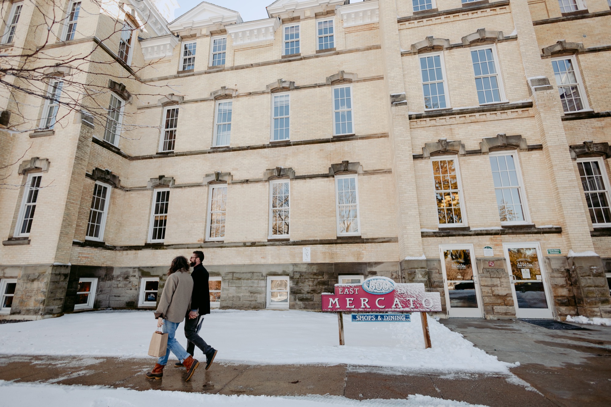 A couple walking hand-in-hand through snowy Grand Traverse Commons