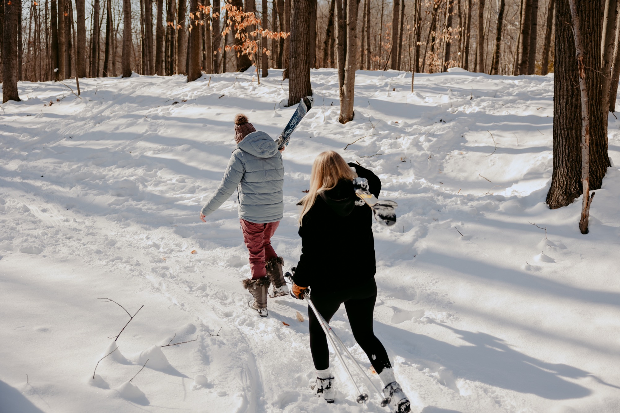 Two people cross-country skiing through a snow-covered hardwood forest