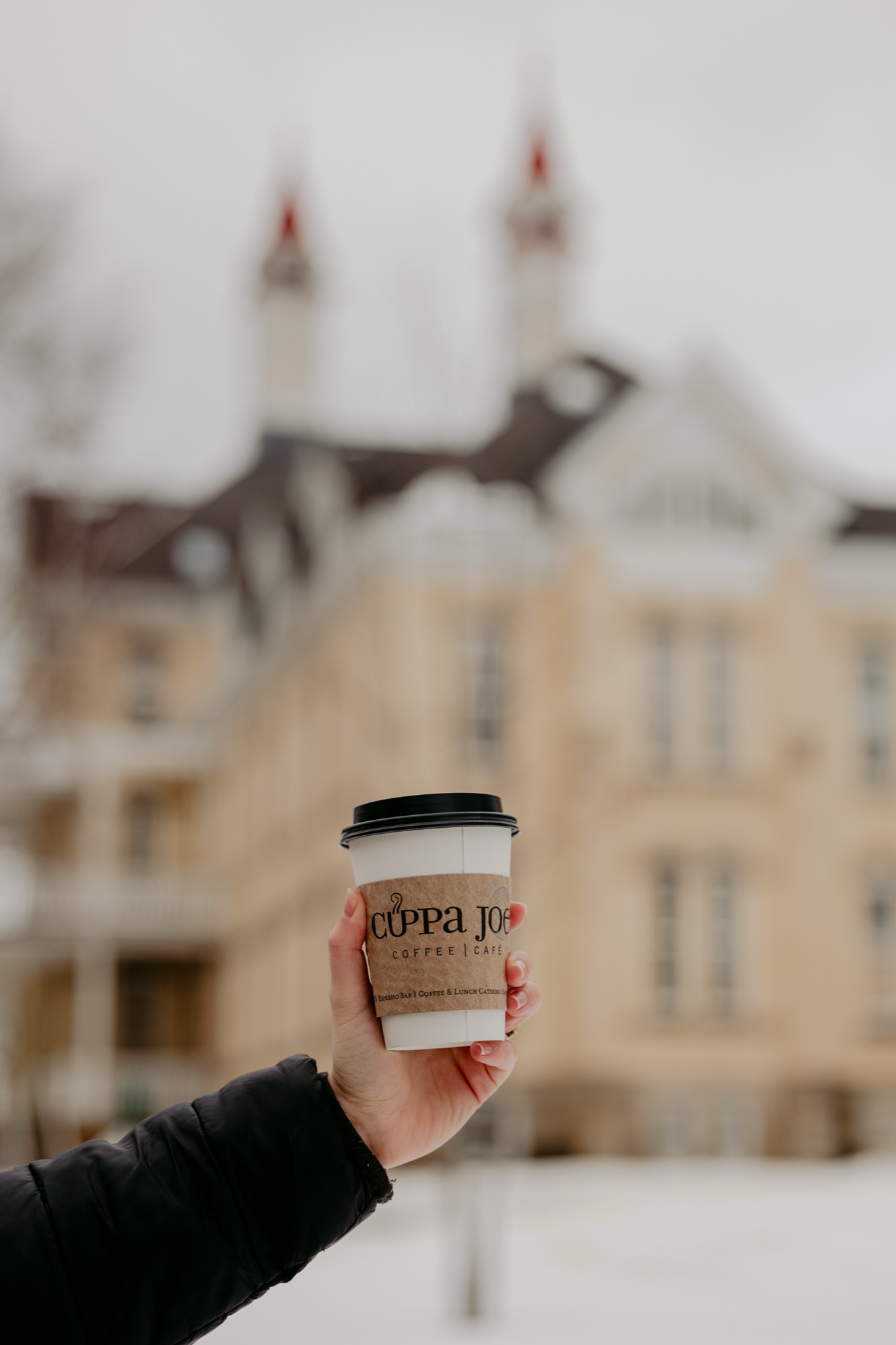 Hand holding a Cuppa Joe coffee cup with snowy downtown Traverse City in the background