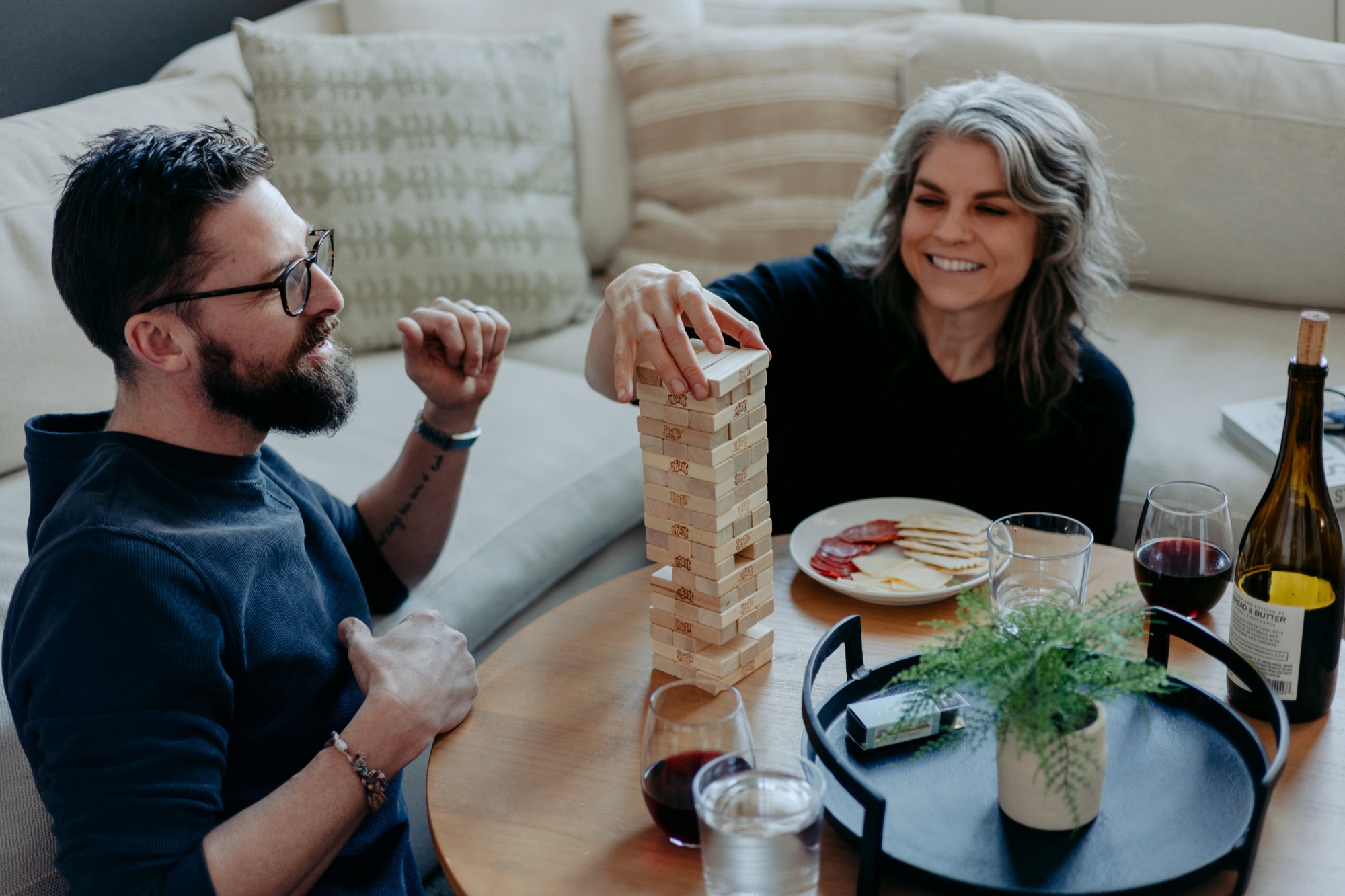 Couple playing Jenga with wine and charcuterie on a cozy evening