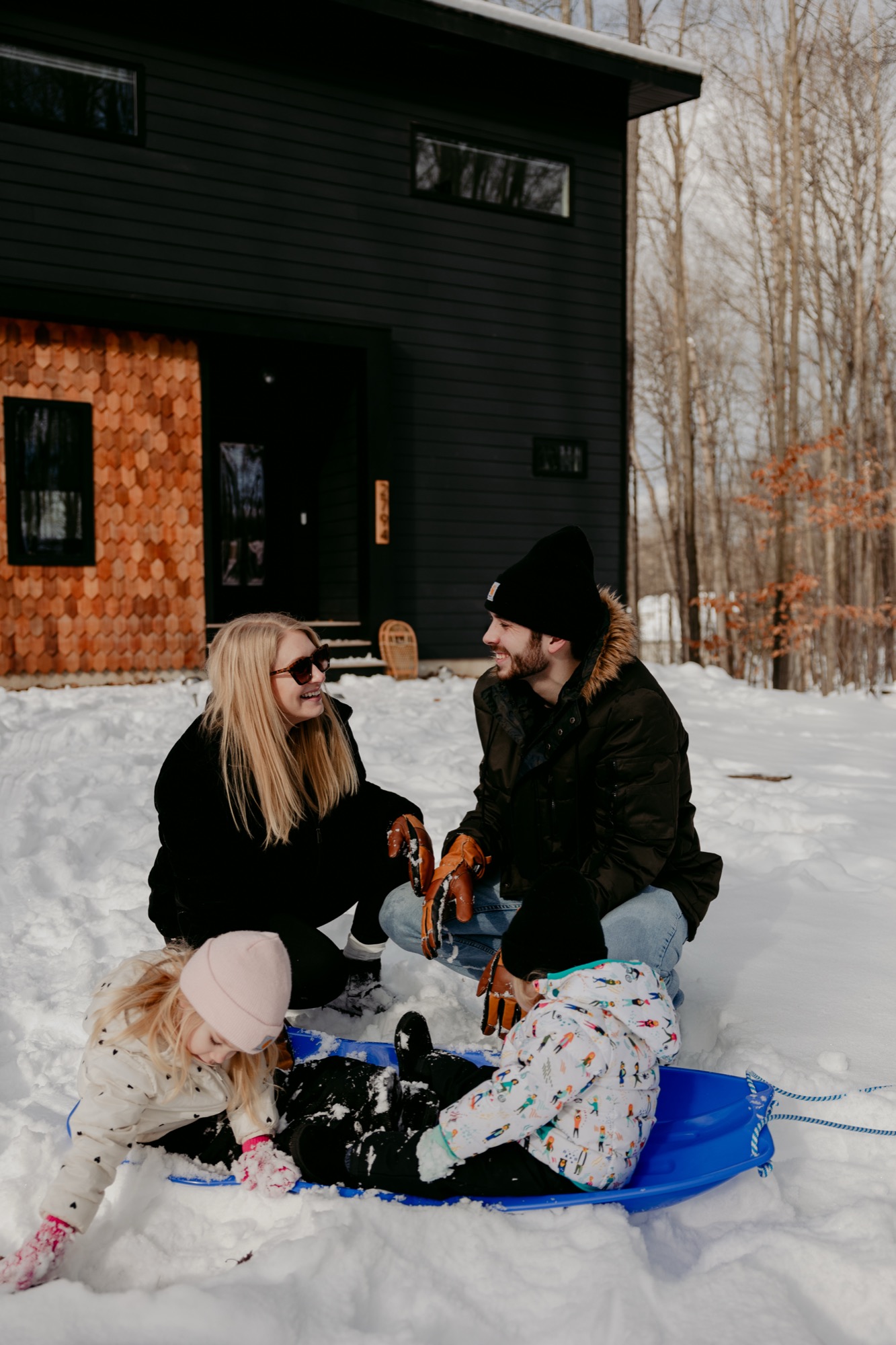 Family sledding in front of the modern Holiday House cabin in the snow
